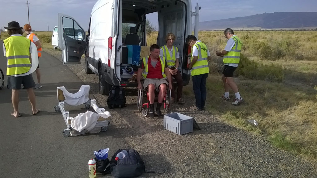 Handcyclists sits in the shade of a van